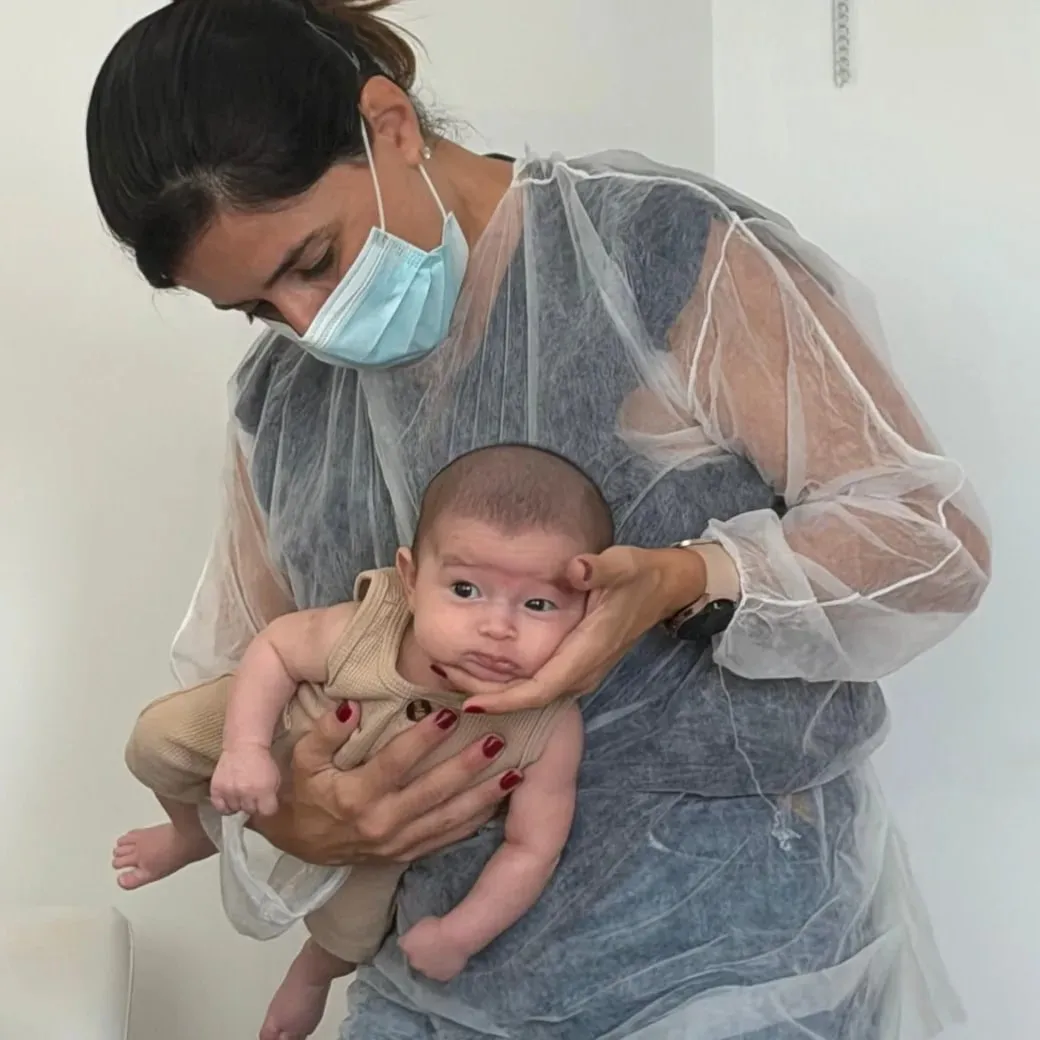 Camila Lemos segurando um bebê no colo e apoiando delicadamente o rosto dele durante o atendimento